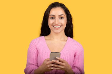 Sosyal medyada akıllı telefon sohbeti yapan, sarı stüdyo arka planında izole edilmiş, mutlu bin yıllık beyaz kadın, kapat. Modern aygıt, blog, internette sörf, iyi haber ve satış