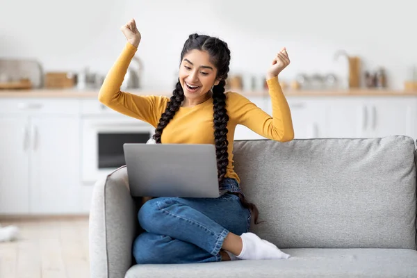 良い知らせだ 自宅でソファに座っている間にノートパソコンで成功を祝う幸せな若いインドの女性 喜びで拳を上げ 興奮して叫んだ千年東の女性 スペースをコピーします — ストック写真