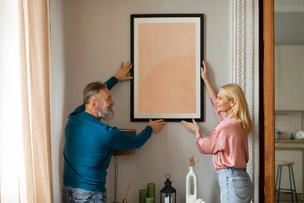 Happy Mature Couple Hanging Picture Frame Wall Together Stående Inomhus — Stockfoto