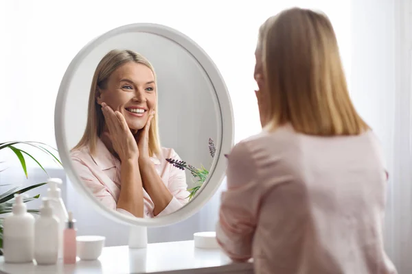 美丽的中年女性看着镜子 摸着脸 笑着欣赏自己的外表 在家里做日常美事 选择焦点的画像 — 图库照片