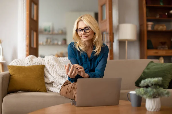 Sarışın Olgun Bir Kadınının Telefondaki Mesajı Evdeki Koltukta Dizüstü Bilgisayarda — Stok fotoğraf