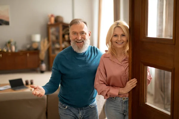 stock image Welcome Home. Joyful Mature Couple Opening Door Of New House, Smiling To Camera Meeting And Greeting You Indoors. Husband And Wife Standing In Doors Of Their Apartment. Own Real Estate