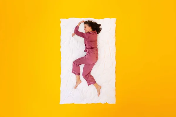 穿着睡衣躺在白色毛毯上躺在黄色工作室的背景下 享受健康睡眠的女人 睡眠常规和娱乐的概念 从上方看 — 图库照片