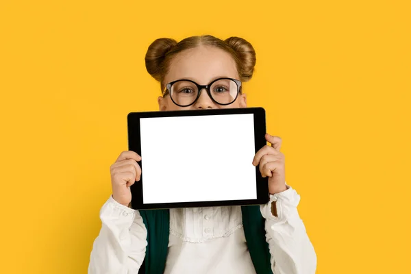 Online Ad. Cute Schoolgirl Holding Blank Digital Tablet With White Screen, Cheerful Preteen Female Kid Advertising New Application Or Website For Study While Posing Over Yellow Background, Mockup
