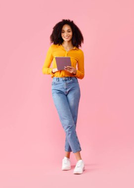 Dijital tablet tutan ve kameraya gülümseyen mutlu siyahi kadın, Afro-Amerikan kadın online alışveriş veya uzaktan öğrenme için modern aletler kullanıyor, dikey çekim