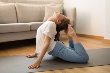 Neşeli Avrupalı genç sporcu kız atlet pilates yapıyor, oturma odasında esniyor. Spor, yoga ve spor evde, antrenman, tek başına egzersiz, reklam ve teklif