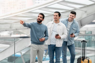 Modern Havalimanı 'nda Üç Gezgin Akıllı Telefonlar Kullanarak Parmak Yanı Yanı Bavulla Duruyor. Yeni Seyahat Uygulaması Reklamı Yolcuları. Turistler için Mobil Hizmetler