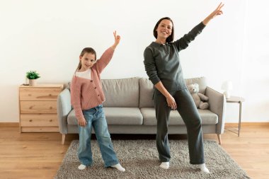 Neşeli Avrupalı bin yıllık anne ve genç kız eğleniyor, dans ediyor, oturma odasında müzik dinliyor, tam boy. Birlikte eğlence, eğlence, aşk, evde ilişki.