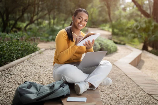 Eラーニング 幸せなブラジルの学生の女性は ノートパソコンを使用してレッスンを準備し ノートを取り 公園の外に座っています 現代の遠隔教育の概念 — ストック写真
