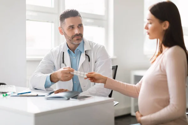 怀孕和医疗概念 中年男性治疗师 给年轻孕妇开处方药 坐在诊所办公室 — 图库照片