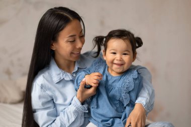 Neşeli Japon Anne ve Sevimli Bebek Kızı 'nın portresi. Evdeki modern yatak odasında gülümseyen kot pantolon giymiş. Bakıcılık ve Çocuk Bakımı Konsepti