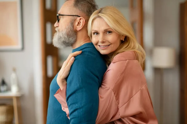 快乐成熟的妻子抱着丈夫站在背后 微笑着在家里拍照 在现代客厅里的配偶拥抱 婚姻幸福 选择性焦点 — 图库照片