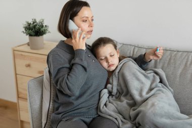 Üzgün Avrupalı bin yıllık anne sakinleşiyor, hasta ergen kıza bakıyor, oturma odasındaki doktorla telefonla konuşuyor. Tedavi için ilaç grip ve soğuk, aşk, evdeki ilişkiler