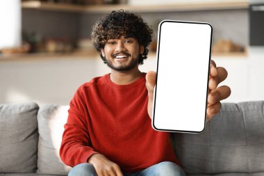 Cep telefonu reklamı. Gülümseyen Hintli adam evde koltukta otururken kamerada büyük beyaz ekranlı boş bir akıllı telefon gösterisi yapıyor. Doğu Yakası Erkek Uygulaması ya da Web Sitesi, Kolaj, Mockup