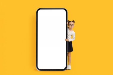 Mobil Teklif. Sevimli küçük liseli kız büyük boş akıllı telefonun arkasından gözetliyor, Eğitimsel Uygulama ya da Web sitesi Tasarımı, Yaratıcı Kolajı için Kopya Alanı 'nı sunan Gülümseyen Kız Çocuk