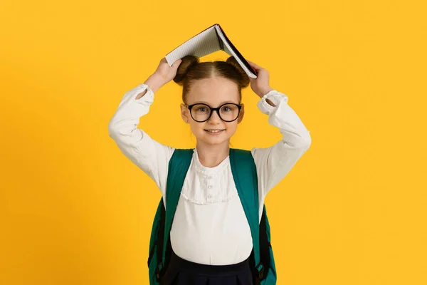 回学校去可爱的小女生手握书本 对着相机微笑 带着背包 带着黄色背景 在演播室里 复制空间里有趣的未成年女生 — 图库照片
