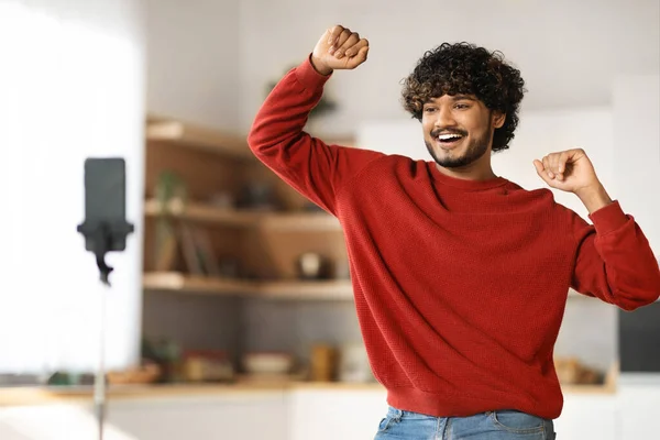 快乐的印度年轻人一边在相机前跳舞一边在家里录视频 积极的东方男人为他的社交网络创造内容 用智能手机在客厅里的三脚架上 复制空间 — 图库照片