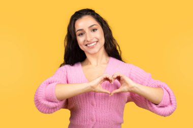 Bin yıllık beyaz kadın elleriyle kalp işareti yapıyor sarı stüdyo arka planında izole edilmiş ilişkilerin tadını çıkarıyor. Aşk, romantizm, insani duygular, minnettarlık, reklam ve teklif