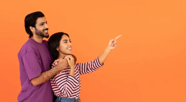 明るく美しい若いですインディアンカップルでカジュアル抱擁 Hindu男と女を探しているとオレンジ色のスタジオの背景に広告のためのフリースペースを指して パノラマ — ストック写真