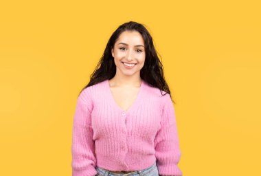 Milenyum ortadoğulu bir bayanın, sarı arka planda, stüdyoda izole edilmiş, gündelik bir şekilde kameraya bakan portresi. Reklam ve teklif, yaşam tarzı, çalışma ve öğrenim