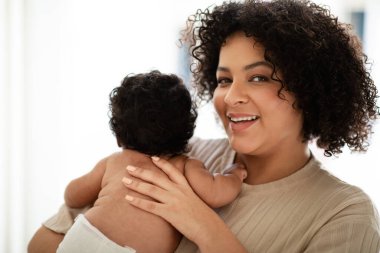 Neşeli bin yıllık Afro-Amerikan kadınları küçük bir çocuğu bebek bezi ile kucaklar, oda içinde tıbbi bakımdan zevk alır. Ebeveynlik, yeni doğana sevgi, evde anne ve çocuk ilişkisi, doğum.