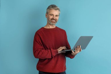 Modern dizüstü bilgisayarı mavi stüdyo geçmişi üzerinden kullanan mutlu, orta yaşlı bir adam web sörfü ya da internette çalışmak, kameraya gülümsemek, kopyalama alanı. Modern teknoloji kavramı