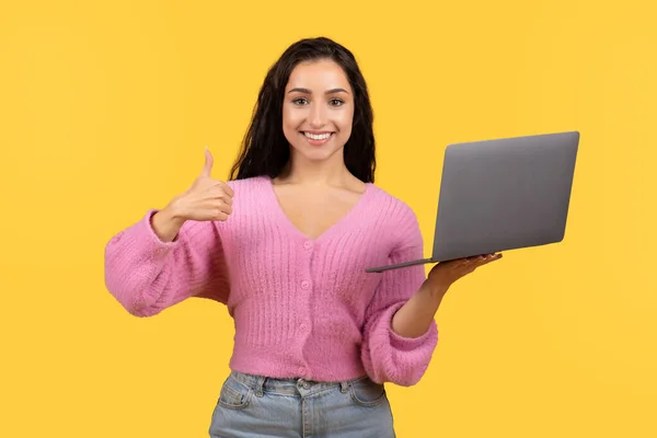 很高兴千禧年女性在笔记本电脑上随意工作 在黄色背景 工作室中表现出孤立的大拇指 远程学习 工作和自由职业 通信方面的建议 小玩意建议 — 图库照片
