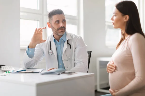 中年男人医生在现代诊所的办公室里为孕妇开药丸或维生素处方 坐在办公桌前聊天 — 图库照片