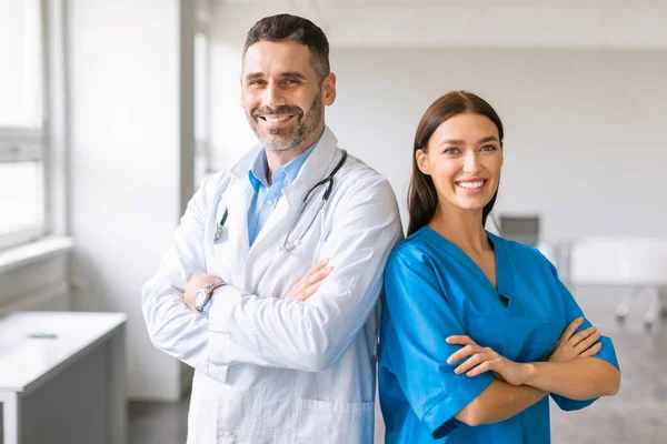 自信的高加索同事 男医生和女护士 身穿外套 双手交叉地摆出姿势 对着现代轻便医务室的摄像机微笑 — 图库照片