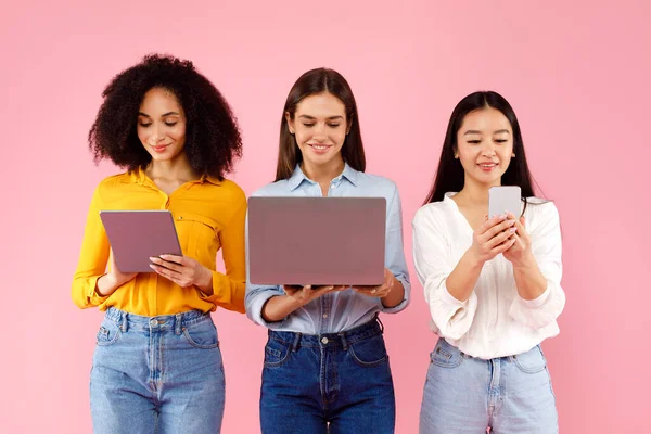 Üç tane çok ırklı kadın cihaz kullanıyor ve ekranlara bakıyor, pembe stüdyo arka planında internette geziniyor. Çevrimiçi sosyal medyada kadın grup ağı