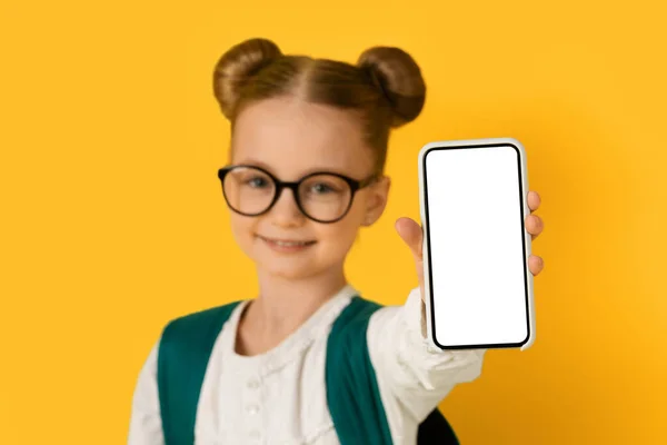 彼女の手で白い画面と空白のスマートフォンを示す眼鏡でかわいい女の子 黄色の背景の上に立ちながら 陽気Preteen女性の子供は新しいモバイルアプリケーションをお勧めします モックアップ — ストック写真