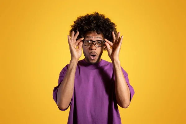 驚くべき成人アフリカ系アメリカ人の男性が口を開けて紫色のTシャツを着て黄色のスタジオの背景に眼鏡を外します 勉強と仕事 ライフスタイル 広告とオファー — ストック写真