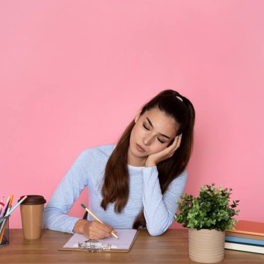 Uykucu, çekici, latin esmer, şık günlük kıyafet giymiş, sekreter, elinde kalem, koluna yaslanmış, yorgun, aşırı çalışılmış, pembe arka plan.