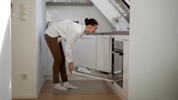 舒适的现代生活 快乐的女人来到厨房 打开洗碗机 把脏盘子放进去就走 享受轻松的家庭生活 跟踪镜头 慢动作 自由自在的空间 — 图库视频影像