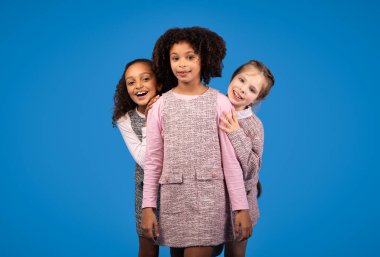 Mavi stüdyo arka planında izole edilmiş kameraya bakan Afro-Amerikan ve beyaz kızlar. Sürpriz, eğlence, çocuk duyguları, çocukluk, reklam ve teklif