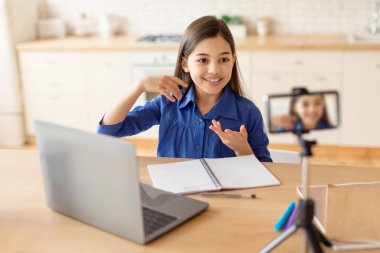 Çevrimiçi Eğitim. Akıllı telefon aracılığıyla video çeken liseli kız dizüstü bilgisayarın başında oturuyor ve evde uzaktan öğreniyor. Telefonla konuşan Ortadoğulu Kız Mesafeli Sınıfta. Seçici Odaklanma