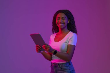 Dijital Boş Zaman. Tablet Bilgisayarlı Mutlu Siyah Kadın, Mor Arkaplanda Neon Işıkta Poz Veriyor, Gülümseyen Afrikalı Amerikalı Kadın Modern Teknolojileri Seviyor, Kopya Boşluğu