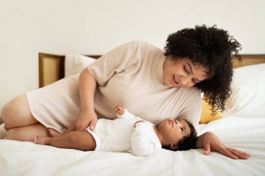 Pozitif genç Afro-Amerikan artı cüsseli kadın ve küçük çocuk yatakta uzanıyor, birlikte rahatlıyor, ilgileniyor, yatak odasının içinde oynuyorlar. Ebeveyn ve bebek, ilişki anne ve bebek, aşk