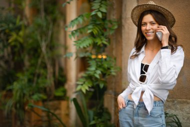 Milenyum tarzı, genç, beyaz kadın turist. Şehirdeki telefon görüşmelerinde şapka takıyor. Hafta sonları macera, iletişim, tatil uygulaması ve tek başına seyahat, bağlantı