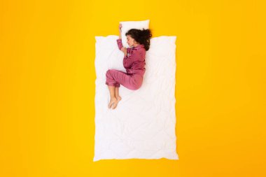 Sağlıklı Uyku Rutini. Battaniye ve yastığın üzerinde uzanan, üzerinde pijamaları olan, Fetal pozisyonda kestirip sarı stüdyonun arka planında uyuyan barışçıl bir bayan. Eğlence ve Konfor Konsepti