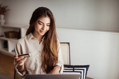 Bilgisayarda yazan neşeli Avrupalı genç bir kadın, kredi kartı kullanıyor, oda içi online alışveriş yapıyor. Finans, para kontrolü, satış, evdeki iş, ödeme emri için aygıt