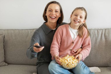 Uzaktan kumandalı mutlu Avrupalı genç kız ve milenyum annesi patlamış mısır yiyor, oturma odasında televizyon izliyor. Birlikte film akşamı, aşk, ilişkiler, evde eğlence.