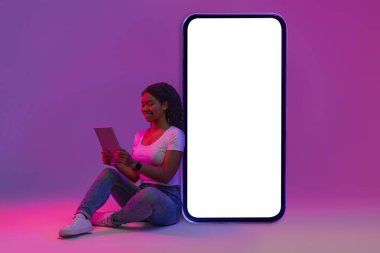 Çevrimiçi reklam. Neon Işığında Büyük Boş Akıllı Telefonun yanında oturan Siyah Kadın, Mor Arkaplan, Kolaj, Model, Mor Makyaj yaparken Modern Gadget Kullanan Mutlu Afrikalı Amerikalı Kadın