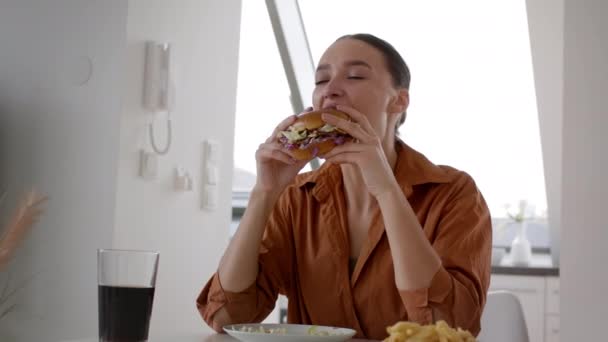 懒散的周末晚餐 年轻漂亮的女人在家里吃饭 愉快地吃着新鲜的汉堡包和薯条 享受着速递食品 跟踪镜头 慢动作 自由自在的空间 — 图库视频影像