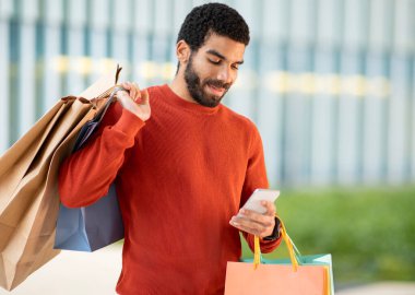 Alışveriş Uygulaması. İçerikli Arap Müşteri Telefon Kullanarak İnternetten Yeni Giysiler Alıyor Uygulamada Bekleme Kağıtları Paketleri Dışarıda. Özellikler ve Ticaret Konsepti