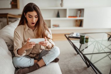 Milenyum Asyalı bayanın telefonda videosu olmasına sevindim. Oturma odasında video görüşmesi var. Sürpriz, iyi haber, online alışveriş uygulaması, sosyal medya sohbeti, reklam ve teklif