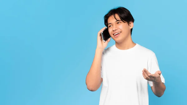 モバイルオファー 明るい韓国のティーン男はブルースタジオの背景の上に携帯電話のポーズで話しています 電話で連絡する学生少年 通信だ 空の空間を持つパノラマ — ストック写真