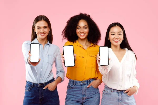 お勧めします モックアップ バナー ピンクのスタジオの背景のための無料のコピースペースを示す 手に白い空白の画面を持つ携帯電話を保持する3つの多人種女性の肖像画 — ストック写真