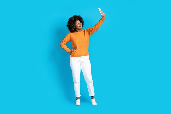 穿着休闲装 带着自拍的年轻黑人女子在智能手机上 与蓝色工作室背景隔离 复制空间 全身上下都是时尚迷人的年轻黑人女性 社交媒体概念 — 图库照片