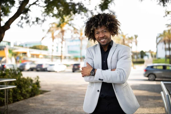 Confident african american middle aged male entrepreneur in suit posing with crossed arms, smiling at camera, standing outdoors. Businessman and startup, business and trade
